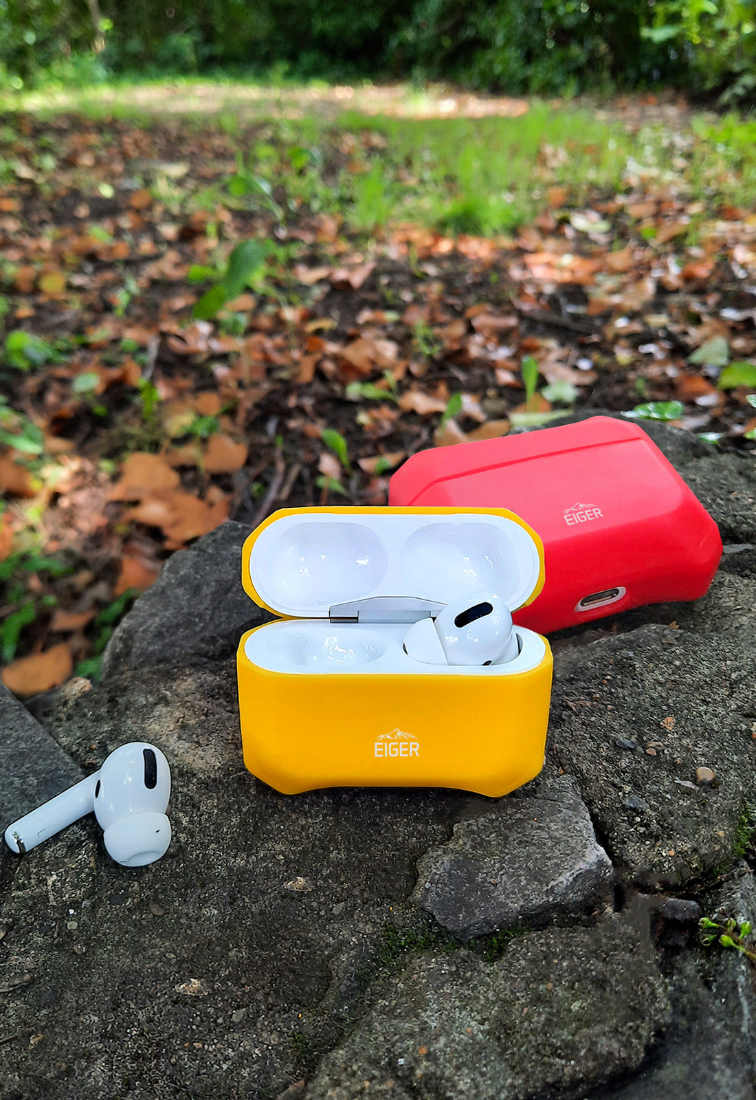 2 sets of airpods outside on rock, each wireless earphone set is in a colourful silicone protective case from eiger in yellow and red